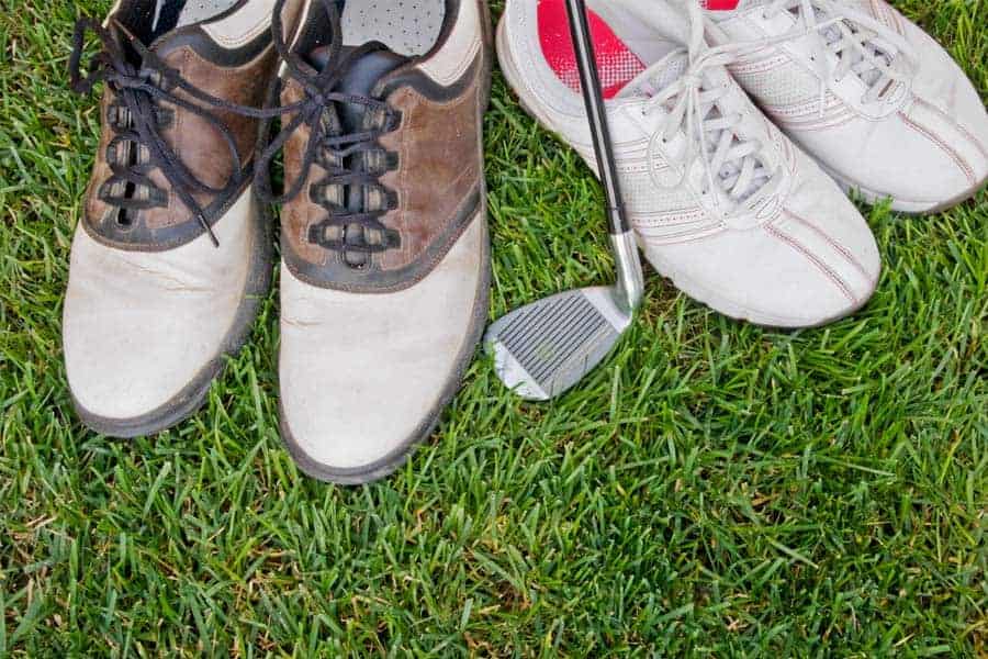 Two pairs of golf shoes placed on a golf course with a club
