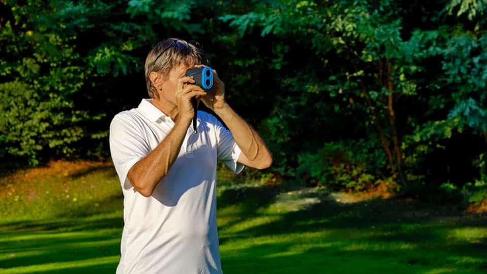 A golfer is seen using the handy golf rangefinder to help gauge distance over the golf course .