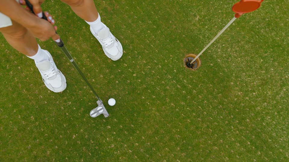 A golfer is standing two feet away from the ball with the putter to put the ball in the hole.