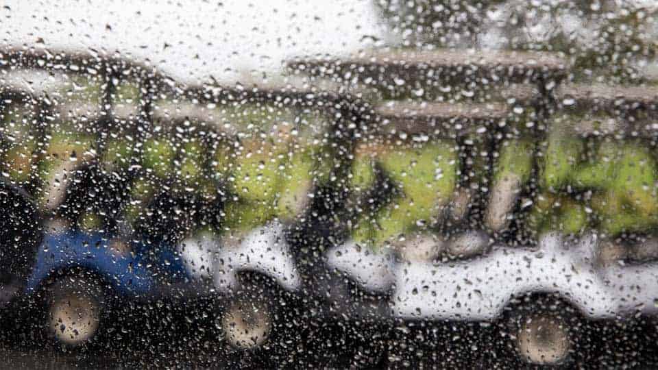 View of the golf carts on the course through a window covered with rain drops.