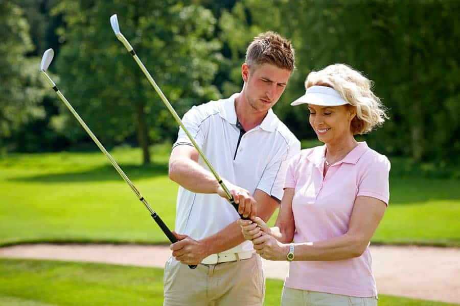 A golf coach is teaching a woman golfer on the techniques of holding the golf club properly