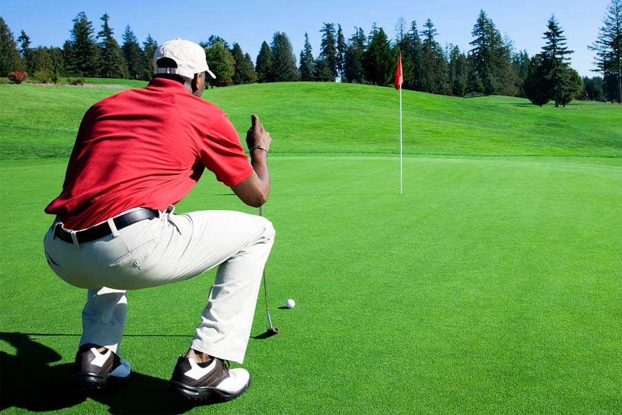A golfer is trying his putt shot correctly in the golf course