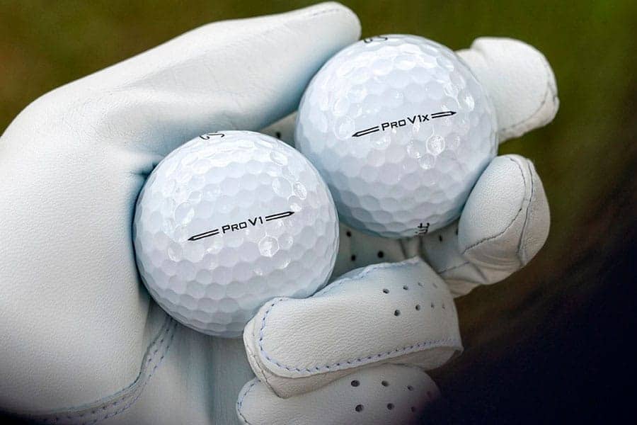 A close up of pro v1 and pro v1x balls in a golfer's hand wearing gloves