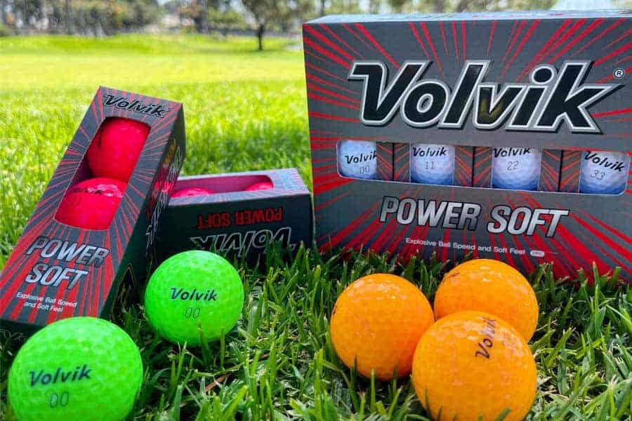 Green and orange colored Volvik Power Soft Golf Balls are placed on green near the packaging