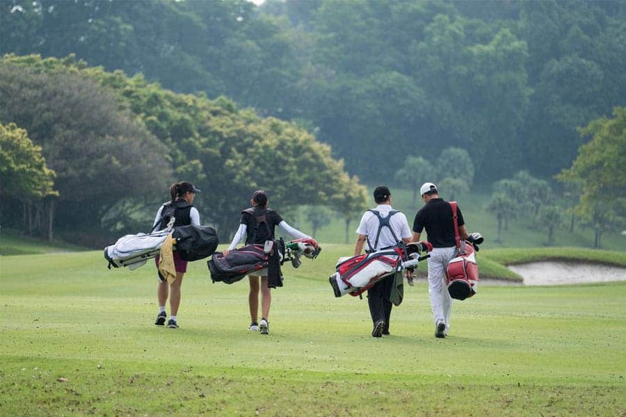 Golfers are walking on the golf course with their golf bags.