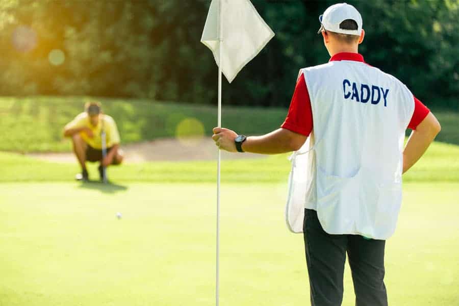 A caddy can be seen holding a flag for the golfer on the golf course.