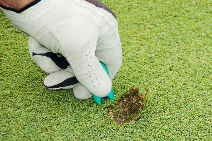 A golfer is seen repairing the course with the help of golf divot tool.