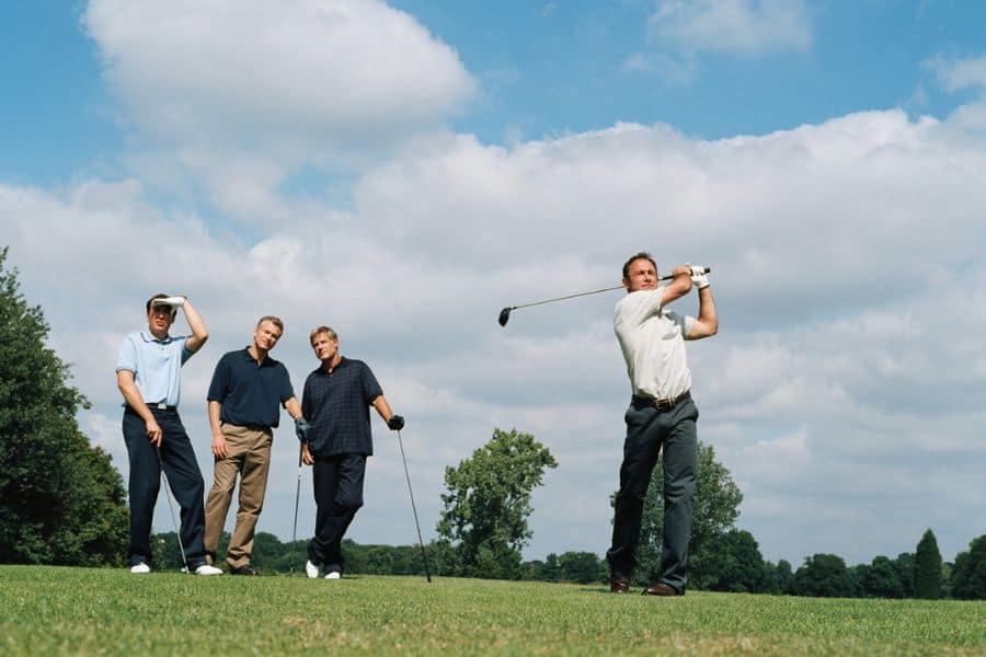 A golfer is hitting a golf shot on the golf course while others are spectating the shot.