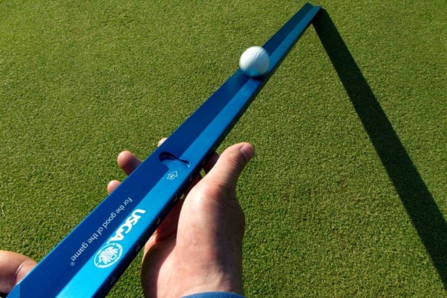 A golfer is measuring on golf course with stimpmeter and a golf ball