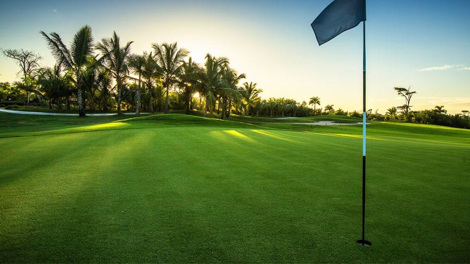 The green tropical land is used for a golf course with flags placed near the holes.
