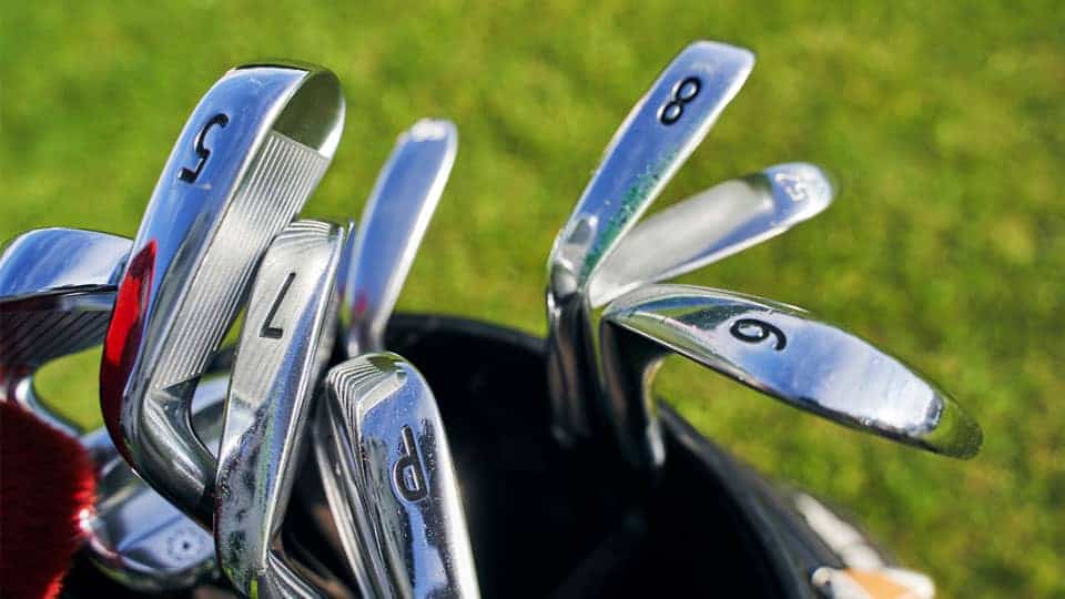 A set of irons ranging from 2 -iron to 9-iron are placed in a golf bag over the course.