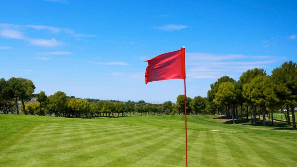 The flag is waving over the golf course due to the strong winds.