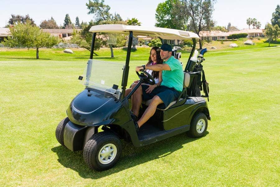 A couple is riding a golf cart in the golf course