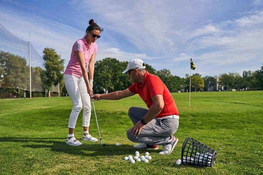 A golf coach assisting a woman golfer in playing golf properly