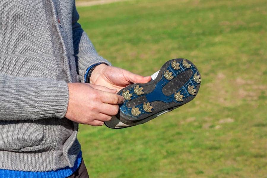 A golfer is holding a golf shoe and trying to remove spikes