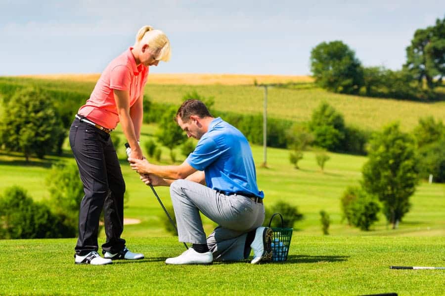 A golf coach is helping a beginner golfer in adjusting the stance.
