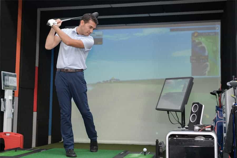 A golfer is practicing the golf game at home with simulators and monitor.