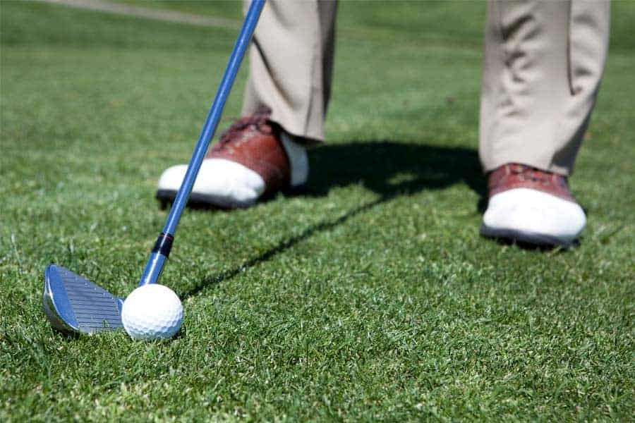 A golfer is hititng the golf ball on the golf course with a golf club.