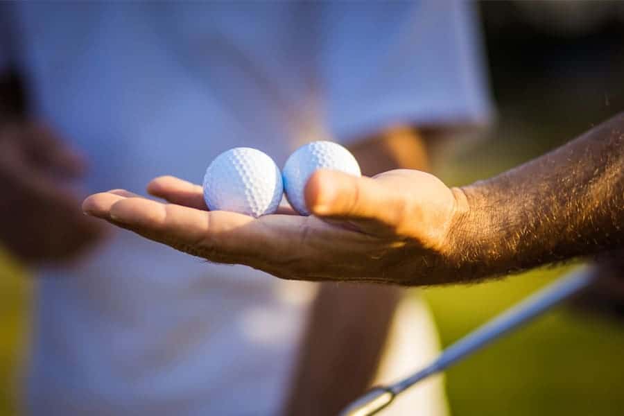 A golfer is holding two golf balls in his hand.
