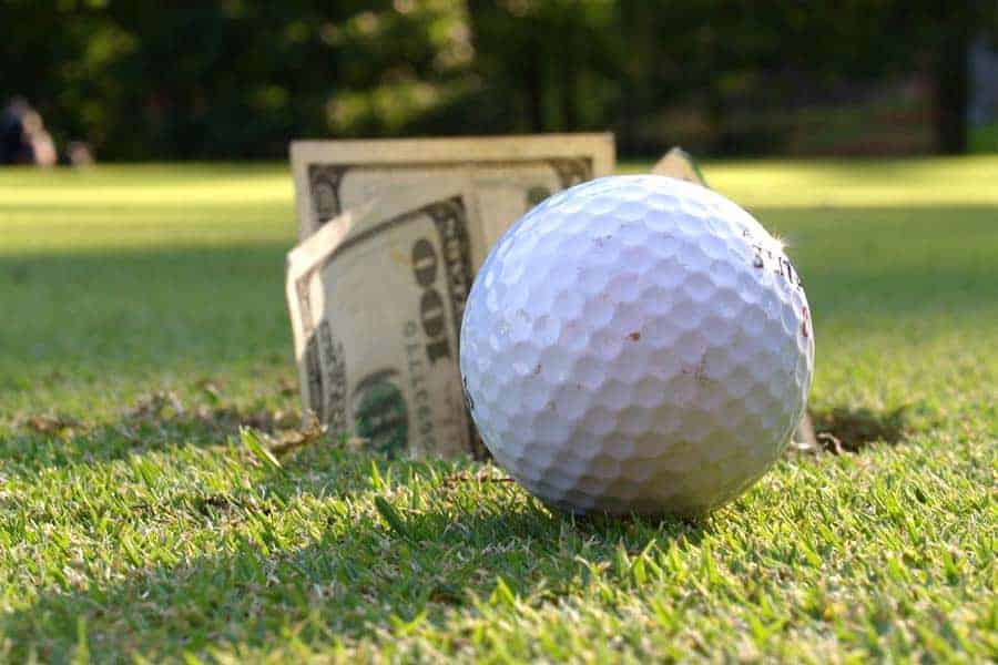 A golf ball is placed near the golf course hole with some money on the greens.