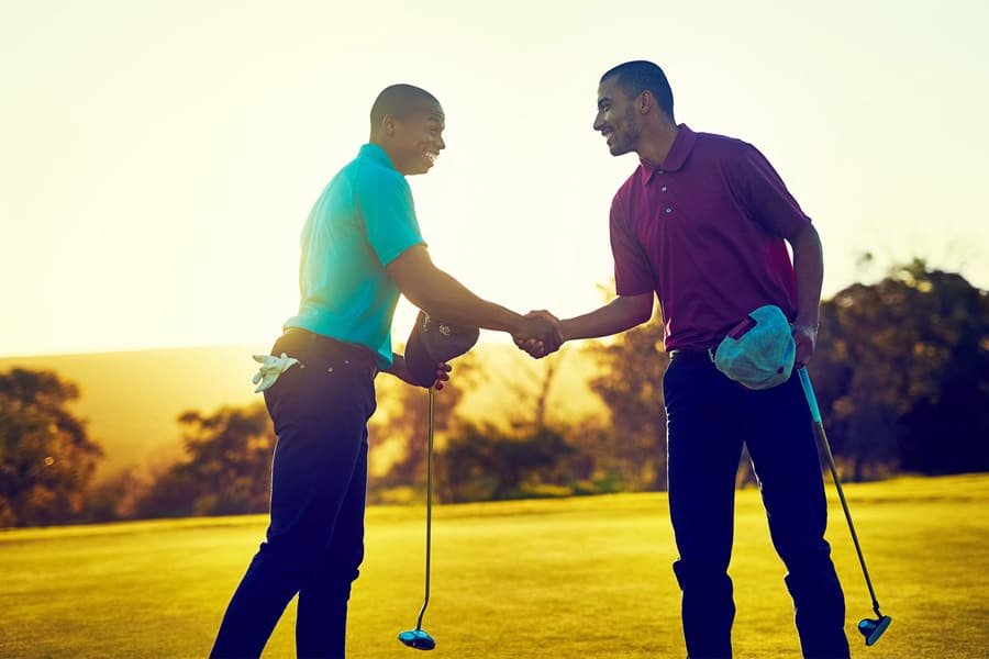 Two golfers are shaking their hands on the golf course after their match play.