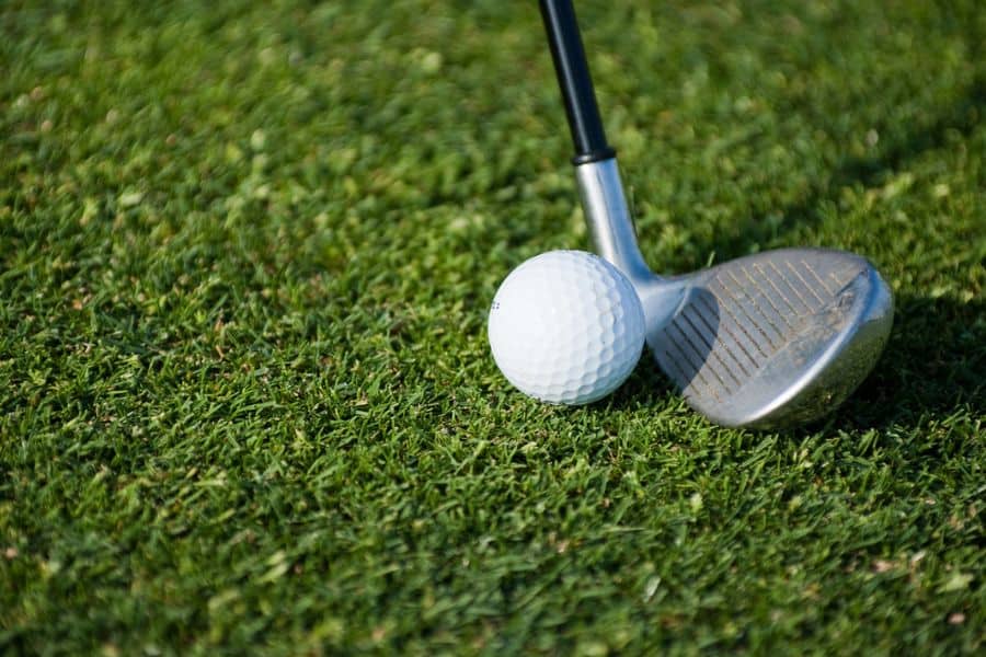 Golf clubhead is near the golf ball on the golf course.